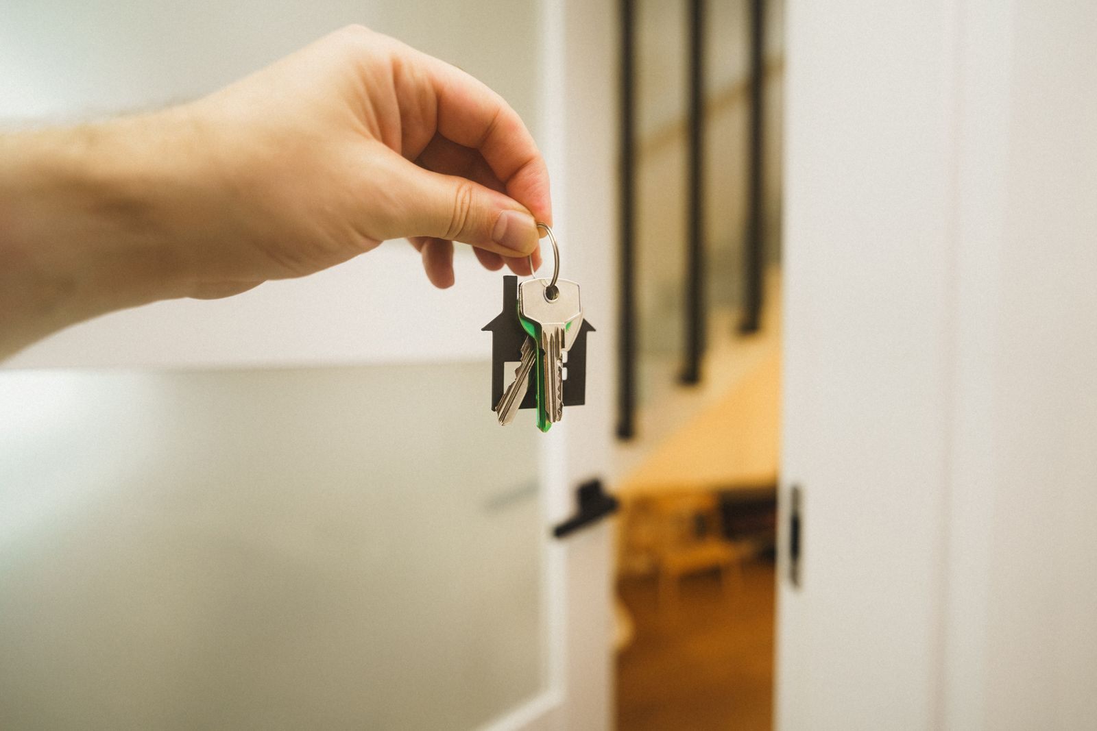 A hand holding a house key indoors signifies new ownership or leasing in real estate